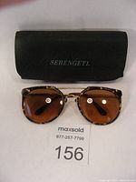 Front view of the sunglasses laid flat with the Serengeti case behind, showing the tortoise shell pattern and brown lenses.