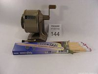 Side view of Apsco Vacuhold pencil sharpener with two boxes of Dixon EnviroStiks pencils stacked in front showing brand and quantity.