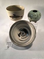 Three Asian pottery pieces arranged with white background, showing overall lot contents: floral tripod vase, fish decorated bowl, and swirled glaze bowl.