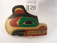 Front view of a carved wood plaque in the shape of a bear head, painted in black, red, green, and natural wood color.