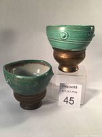 Two Jim Etzkorn ceramic goblets side by side showing overall shape and color contrast between metallic bronze base and turquoise upper bowl.