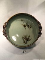 Top-down view showing the oval porcelain dish interior with hand-painted bamboo leaves and stems design, green glaze and brown accent rim and handles.