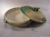 Diagonal view of the ceramic casserole dish with lid slightly open showing interior and exterior glaze with subtle green shading and handle details.