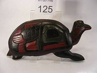 Side view of wooden turtle carving showing painted shell and head details in red, green, and black.