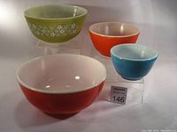 Four vintage Pyrex mixing bowls in different colors and patterns displayed on acrylic risers