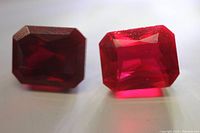 Two rectangular emerald-cut red gemstones side by side on a white surface