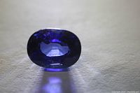 Front top view of deep blue oval sapphire with faceted surface showing internal clarity and color.
