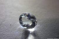 Oval cut clear aquamarine gemstone shown from an angle highlighting its clarity and faceting, placed on a plain surface with focused lighting.