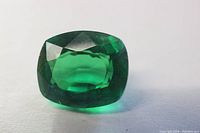 Close-up photo of cushion cut green garnet loose gemstone showing deep green color and facets.