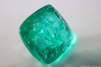 Close-up image showing the cushion cut emerald with visible internal inclusions and facets reflecting light.