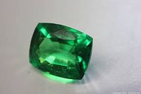 Close-up front angled view of the natural cushion cut green Tsavorite Garnet loose gemstone showing its brilliant green coloration and facets.