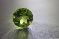Close-up photo of a light green round cut Peridot loose gemstone showing facets and clarity.