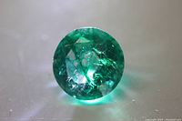 Top view of the round cut natural emerald gemstone with visible internal inclusions and rich green color.