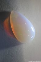 Pear shaped translucent white opal cabochon with rainbow fire play of color resting on a surface, showing depth and color play in side lighting.