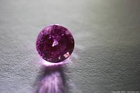 Loose round cut pink sapphire gemstone photographed on a flat surface showing color and transparency.
