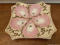 Top-down view of antique majolica oyster plate showing pale pink oyster shapes and gold painted seaweed/coral design on cream background.