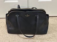Front view of black Kate Spade handbag with double shoulder straps and gold zipper