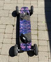 Full top view of the skateboard showing cosmic graphic deck with black grip tape, two black F1 Velcro bindings, and large off-road tires.