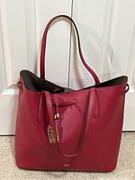 Front view of red Ralph Lauren leather tote bag hanging from two straps showing drawstring detail and RL logo tag.