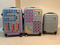 Front view of three Heys hard case luggage pieces in silver with colorful dot patterns, arranged from largest to smallest.