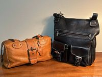 Overview of both handbags showing black shoulder bag and tan satchel side by side