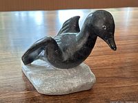 Full side view of the dark soapstone carved duck on a gray soapstone base, showing profile and glaze.