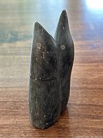 Front view of abstract Inuit soapstone sculpture depicting two seals with worn black surface and carved circular eyes.