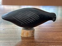 Side view of black soapstone bird on whale bone base
