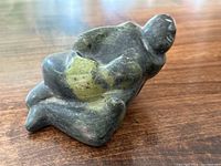 Side view showing the green soapstone figure of a man holding a baby with visible natural stone color variations and smooth surface.