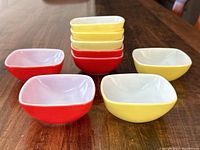 Set of nine vintage Pyrex ovenware bowls stacked and arranged showing four red and five yellow bowls on a wooden surface.