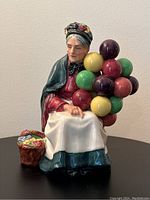 Front view of the Royal Doulton The Old Balloon Seller figurine showing the woman seated holding colorful balloons and a basket of balloons at her side.