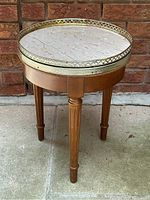 Front view of round wooden side table with travertine top and brass gallery edge