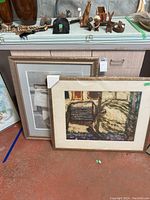 Two framed pieces of artwork leaning against a cabinet, showing frames and protective corners.