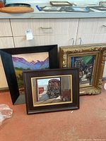 Three framed paintings displayed together leaning against a cabinet