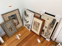 Seven Asian style framed art prints leaned against a wall on wood floor, some prints showing signs of mildew, frames include bamboo styled and metal black frames, sizes vary.