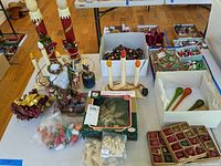 Table with assorted vintage Christmas decorations including electric candle tree toppers, garlands, Santa figurines, and packaged ornaments.