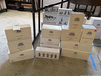 Twelve boxed Department 56 Heritage Village Collection accessories arranged in three stacks showing different box sizes and titles including Dover Coach, Kings Road Cab, Blacksmith, and more.