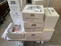 Stack of six white boxes labeled Heritage Village Collection, Dickens' Village Series, some opened to reveal ceramic miniature houses and electrical cords.