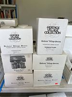 Photo of six white boxes labeled Heritage Village Collection Dickens' Village Series by Department 56. Boxes for Thomas Kersey Coffee House, Kingsford's Brew House, Theatre Royal and others stacked together.