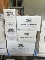 Stacked boxes from Department 56 Dickens' Village Series with visible titles identifiying five different village houses in original packaging.