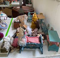 Overall view of hand painted doll furniture with bedding, dolls, and various accessories on white table.