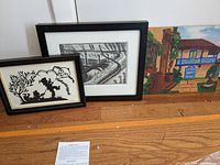 Three framed works on floor: scherenschnitte, graphite drawing, oil painting