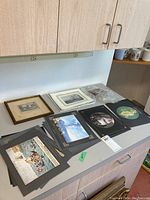 Overview of multiple Italian artwork prints and photos on a gray countertop, including one framed piece, some are portrayal of people and maritime scenes.