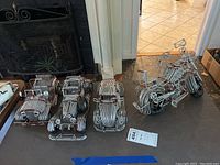Four wire vehicles including three cars and one motorcycle, all made from silver-colored metal wire with detailed construction.