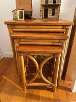 Full view of the three stacked bamboo nesting tables with wooden tops and bamboo frames, including scenic miniature house decorations on the largest table.