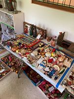 Wide view of ornaments spread on a table with figurines on the shelf behind, showing variety of materials and styles.