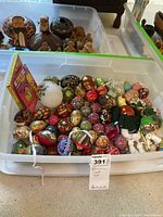 Bin of assorted hand painted Ukrainian style decorative eggs, various colors and designs, with a box and figurines visible in back.