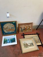 All five framed art pieces on floor including paintings, prints, and one in a decorative black metal frame