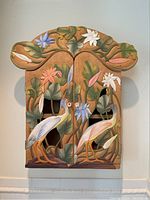 Front view of closed cabinet showing painted crane and floral design on doors and scalloped top.