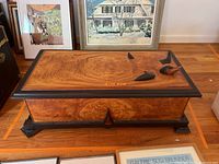 Front and top perspective of trunk showing burl veneer panels, black trim, lid closed and duck finial pieces on top
